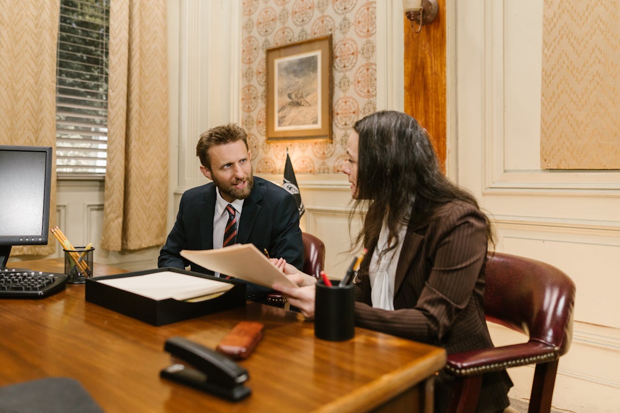creative-03 Two professionals engaged in a business discussion in an office setting, reviewing legal documents.